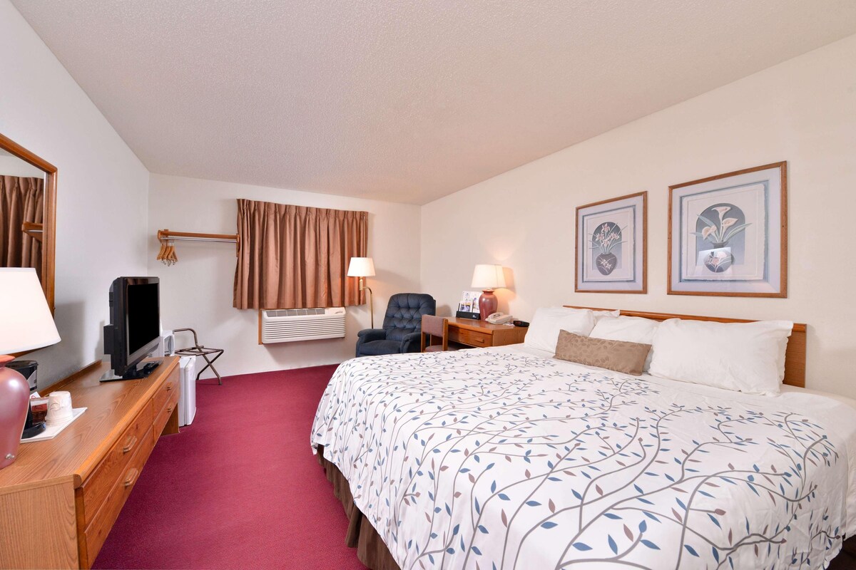 A hotel room with a large bed, a desk with a computer, a chair, a TV, and two framed pictures on the wall.