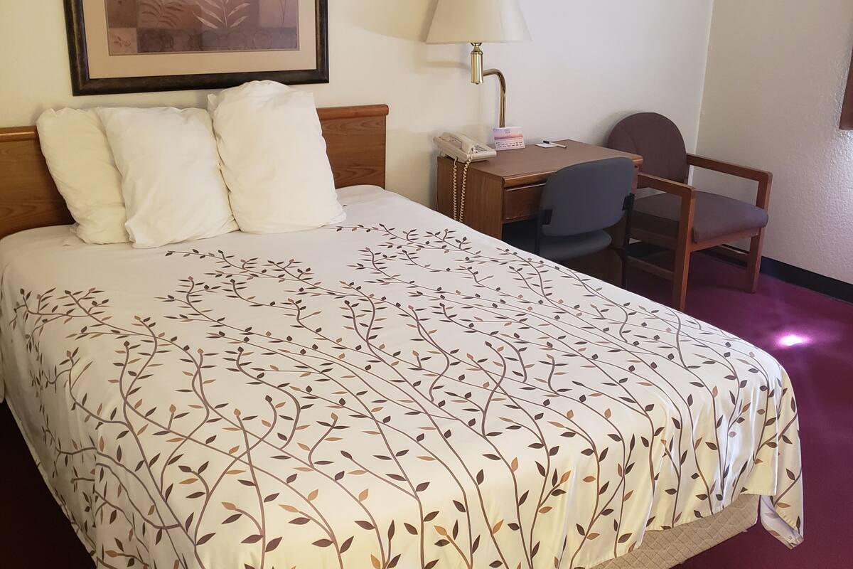A hotel room with a bed, a desk, a chair, a lamp, and a framed picture on the wall.