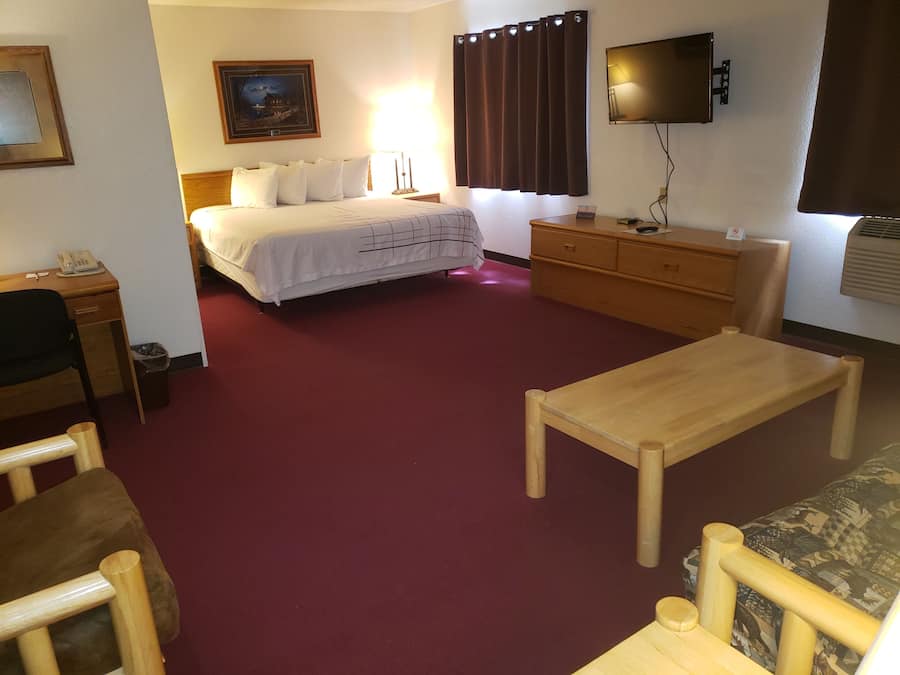 A hotel room with a bed, a wooden desk, a television, a dresser, and a sofa.