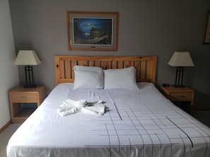 Ein Hotelzimmer mit einem Holzkopfende, zwei Nachttischen mit Lampen, einem Bild an der Wand und einem ordentlich bezogenen Bett mit einem Handtuch.