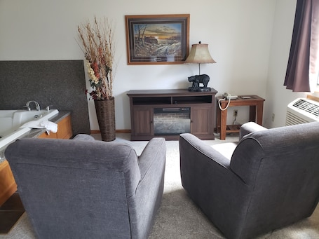 A living room with a sofa, a fireplace, a lamp, a painting, and a vase with branches.