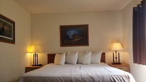 A hotel room with a large bed, two bedside lamps, a framed picture on the wall, and a window with curtains. - Americas Best Value Inn & Suites International Falls (International Falls)