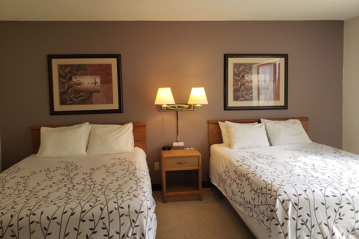 A hotel room with two beds, a nightstand, a lamp, and framed artwork on the walls.