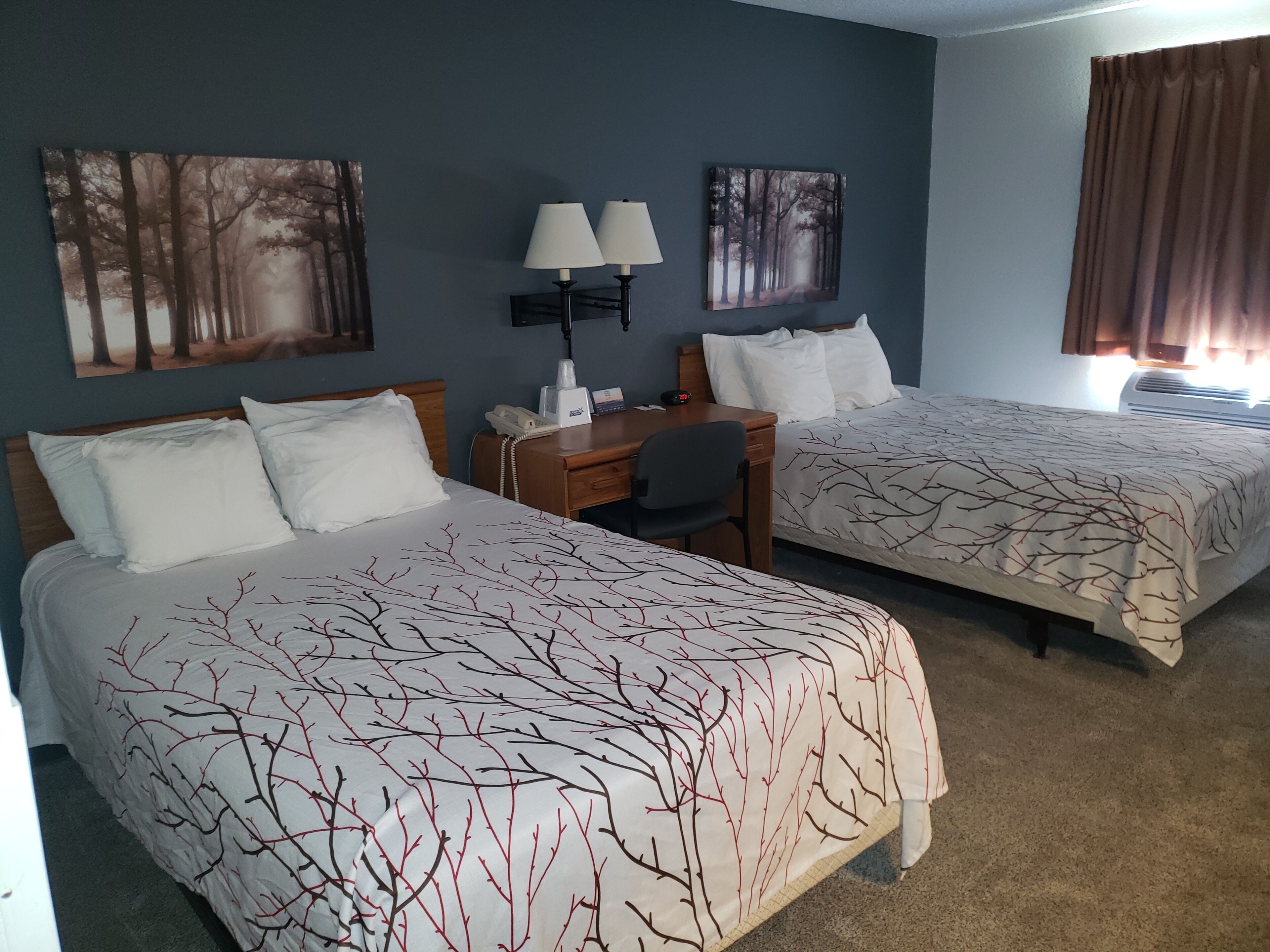 A hotel room with two beds, a desk, a chair, a telephone, and two wall-mounted lamps.