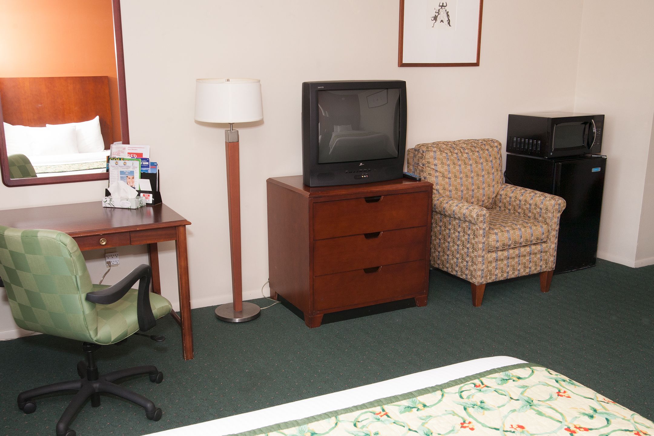 A hotel room with a bed, a desk with a computer, a chair, a television, and a refrigerator.