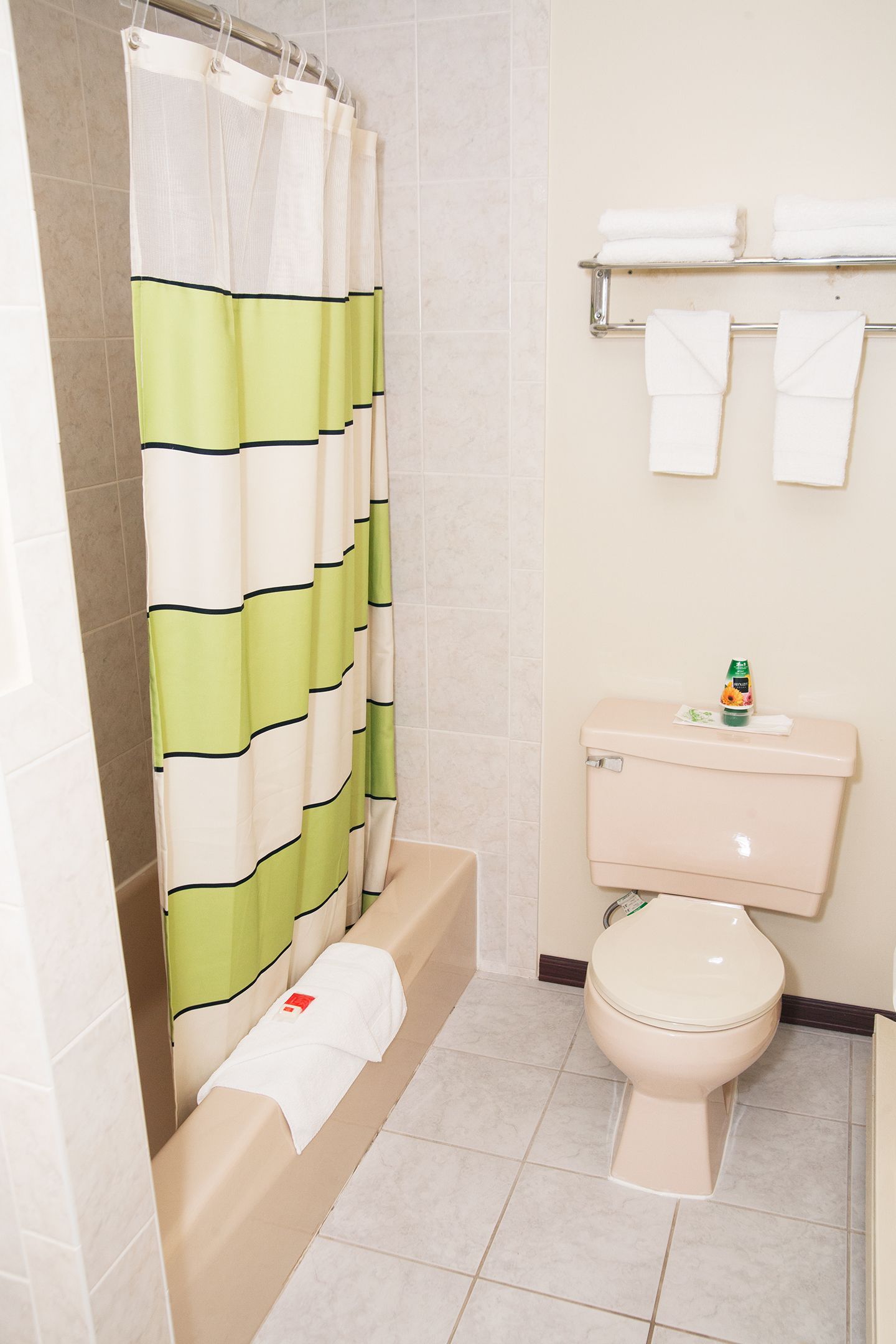 A bathroom with a shower curtain, a toilet, a bathtub, and a towel rack with towels.