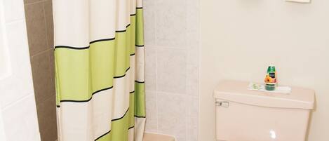 A bathroom with a shower curtain, a toilet, a bathtub, and a towel rack with towels.