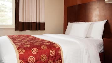 A hotel room with a neatly made bed, a wooden headboard, and a window with curtains.