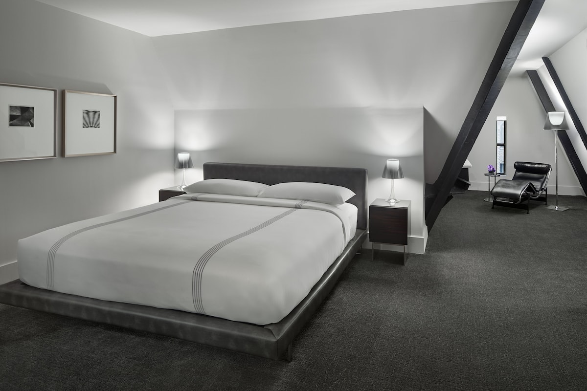 A modern hotel room with a large bed, two bedside tables, a chair, and a desk.