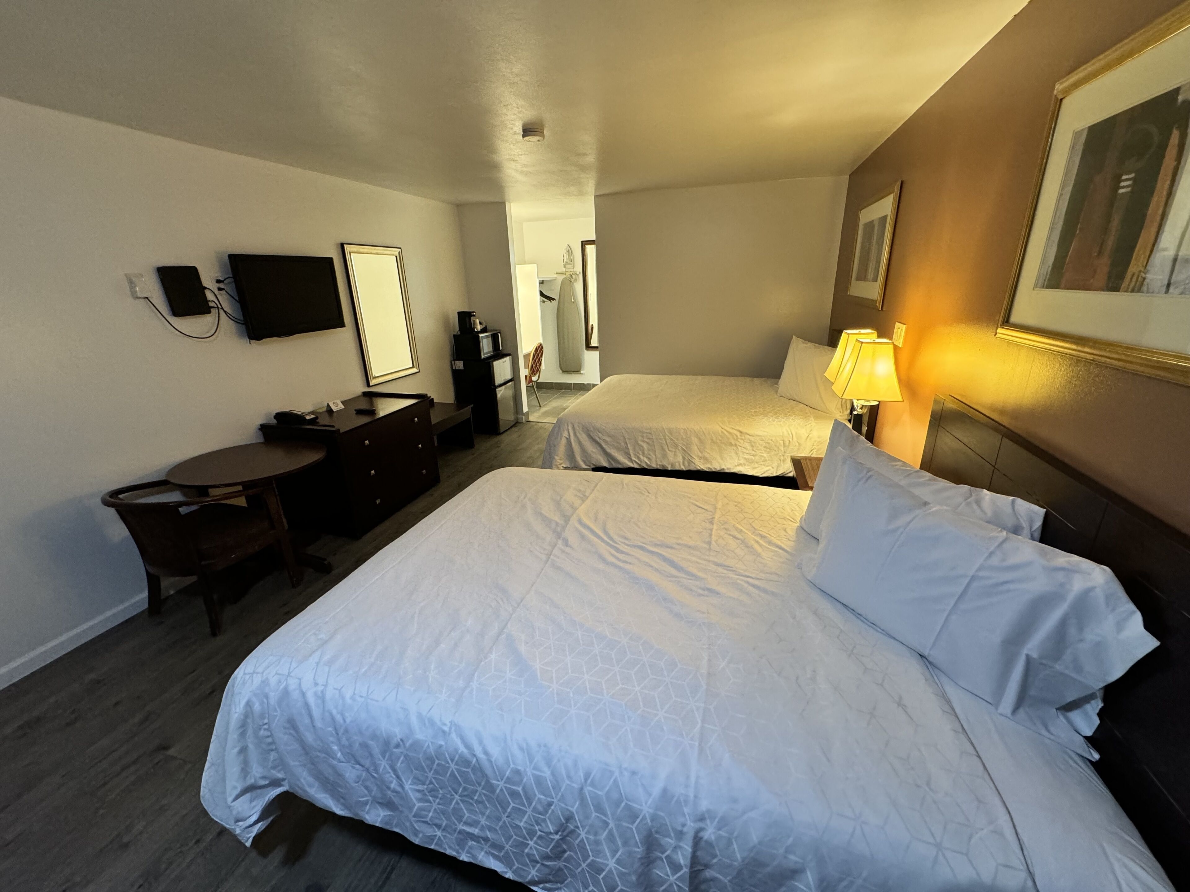 A hotel room with two beds, a desk, a chair, a TV, and a lamp.