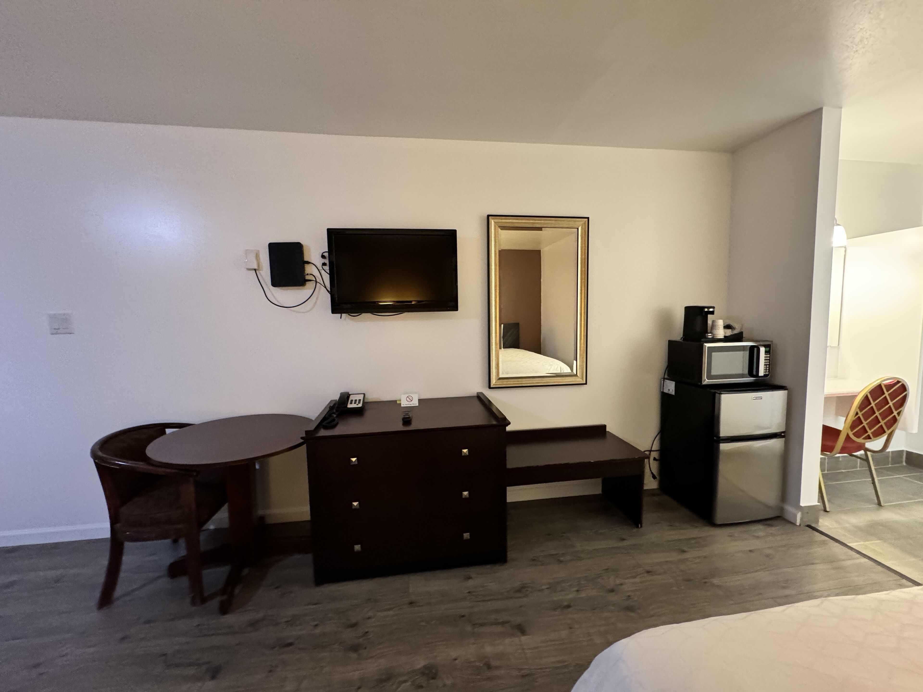 Une chambre d’hôtel équipée d’un bureau, d’une chaise, d’un miroir, d’une télévision, d’un four à micro-ondes et d’un réfrigérateur.
