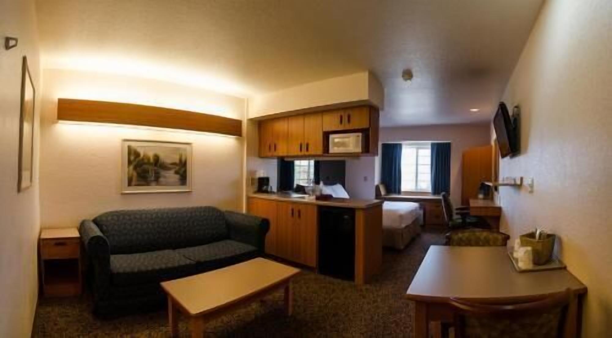 A compact room with a sofa, a small table, a kitchenette, and a bed.