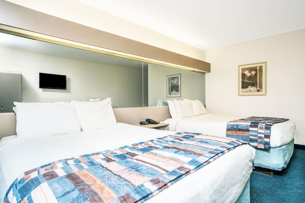 Een hotelkamer met twee bedden, een nachtkastje met telefoon, een spiegel en een klein krukje met sprei.