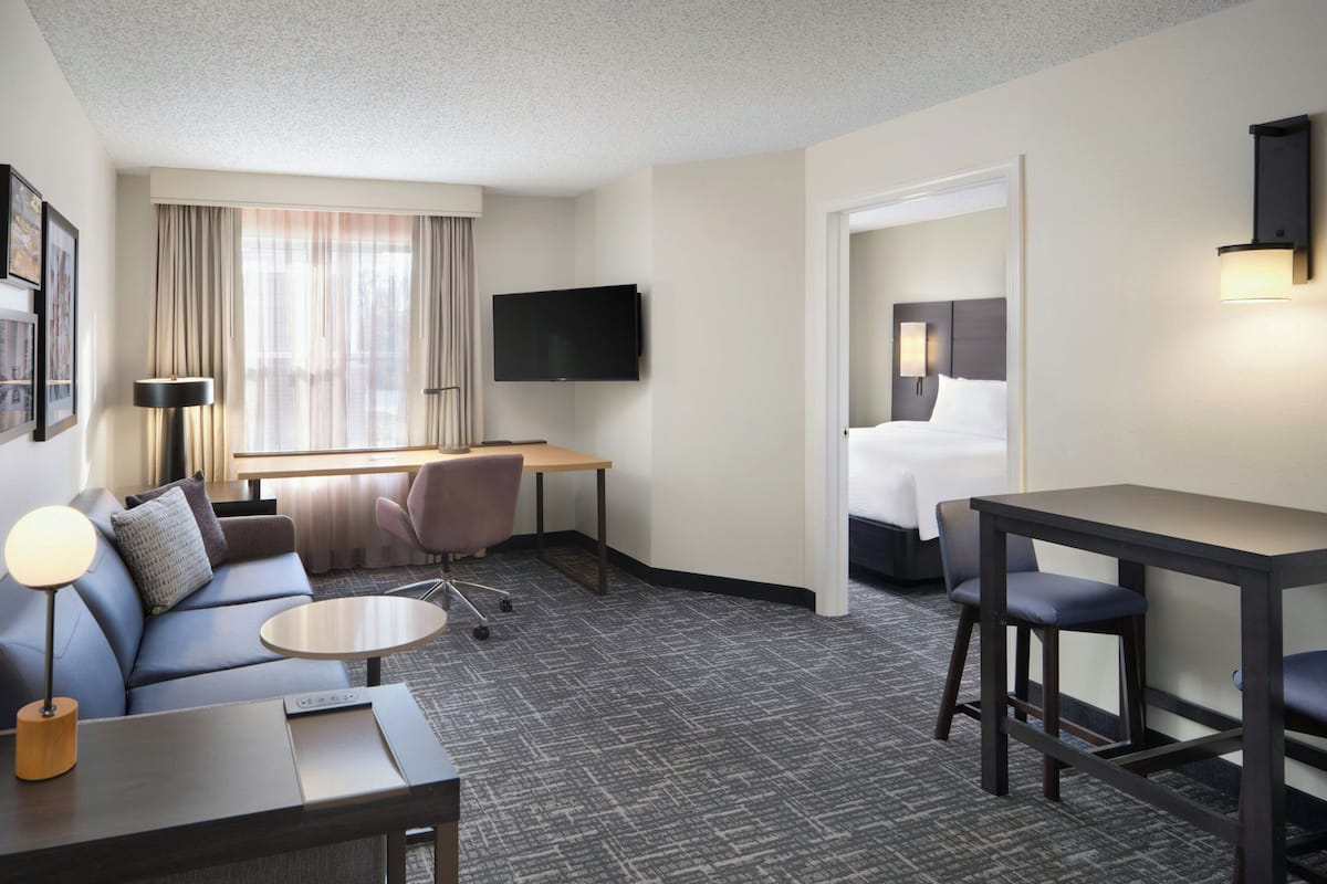 A hotel room with a sofa, a desk, a flat-screen TV, a bed, and a small table.