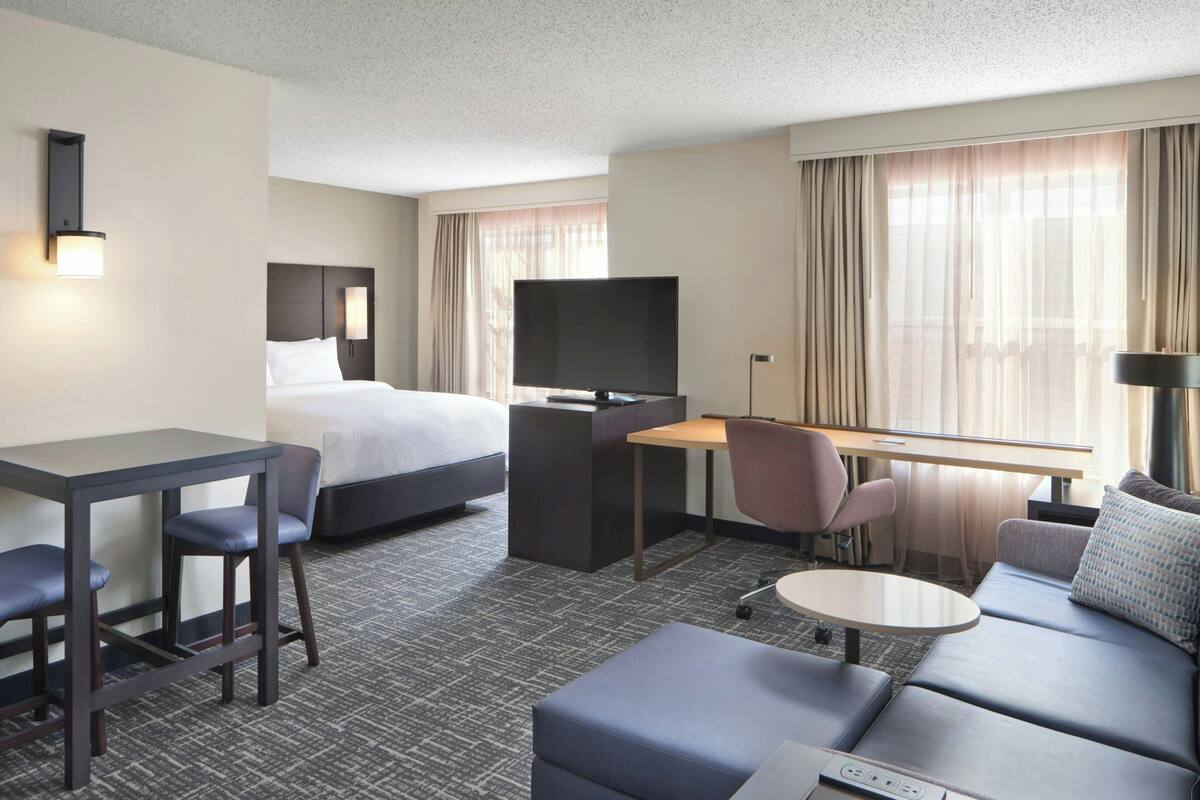 A hotel room with a bed, a desk with a TV, a sofa, and a small table.