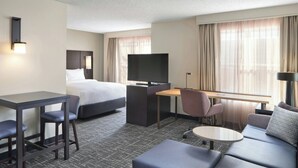 Una habitación de hotel con cama, escritorio con televisor, sofá y una mesita.