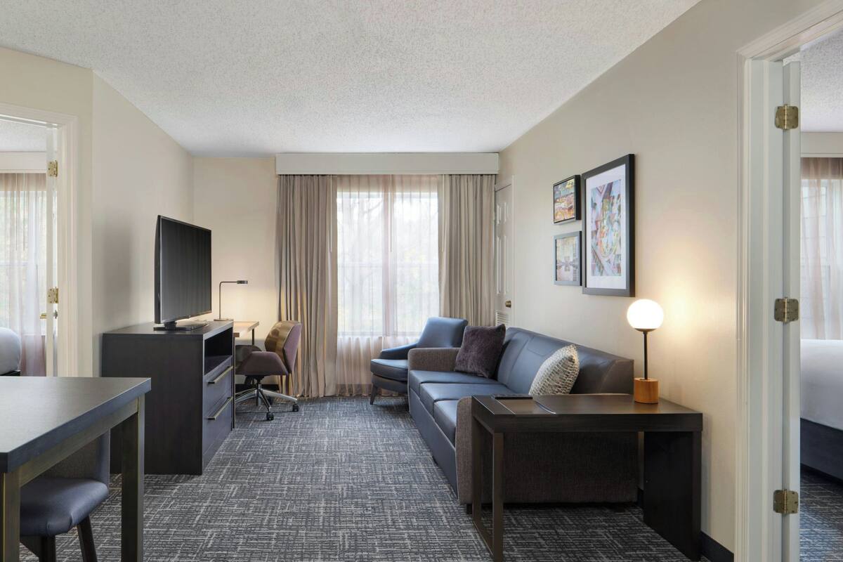 A hotel room with a flat-screen TV, a sofa, a desk, and a lamp.