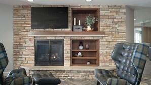 Una sala de estar con chimenea de piedra, un televisor de pantalla plana montado encima y sillones de cuero con tapicería escocesa.