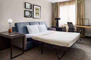 Una habitación de hotel con cama, escritorio, silla y lámpara.