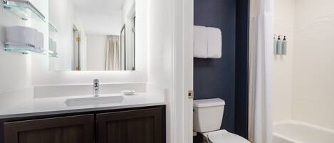 A modern bathroom with a white sink, dark wooden cabinets, a white toilet, and a bathtub.