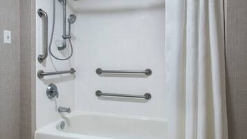 Un baño con una bañera blanca, barras de apoyo y un cabezal de ducha.