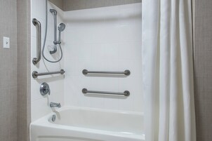 Un baño con una bañera blanca, barras de apoyo y un cabezal de ducha.