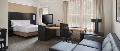 A hotel room with a bed, a desk with a computer, a TV, a couch, and a window with curtains.