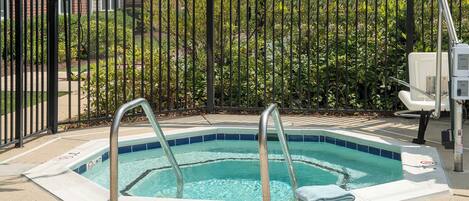 A hot tub with metal railings and a towel on the edge, surrounded by a fence and greenery.