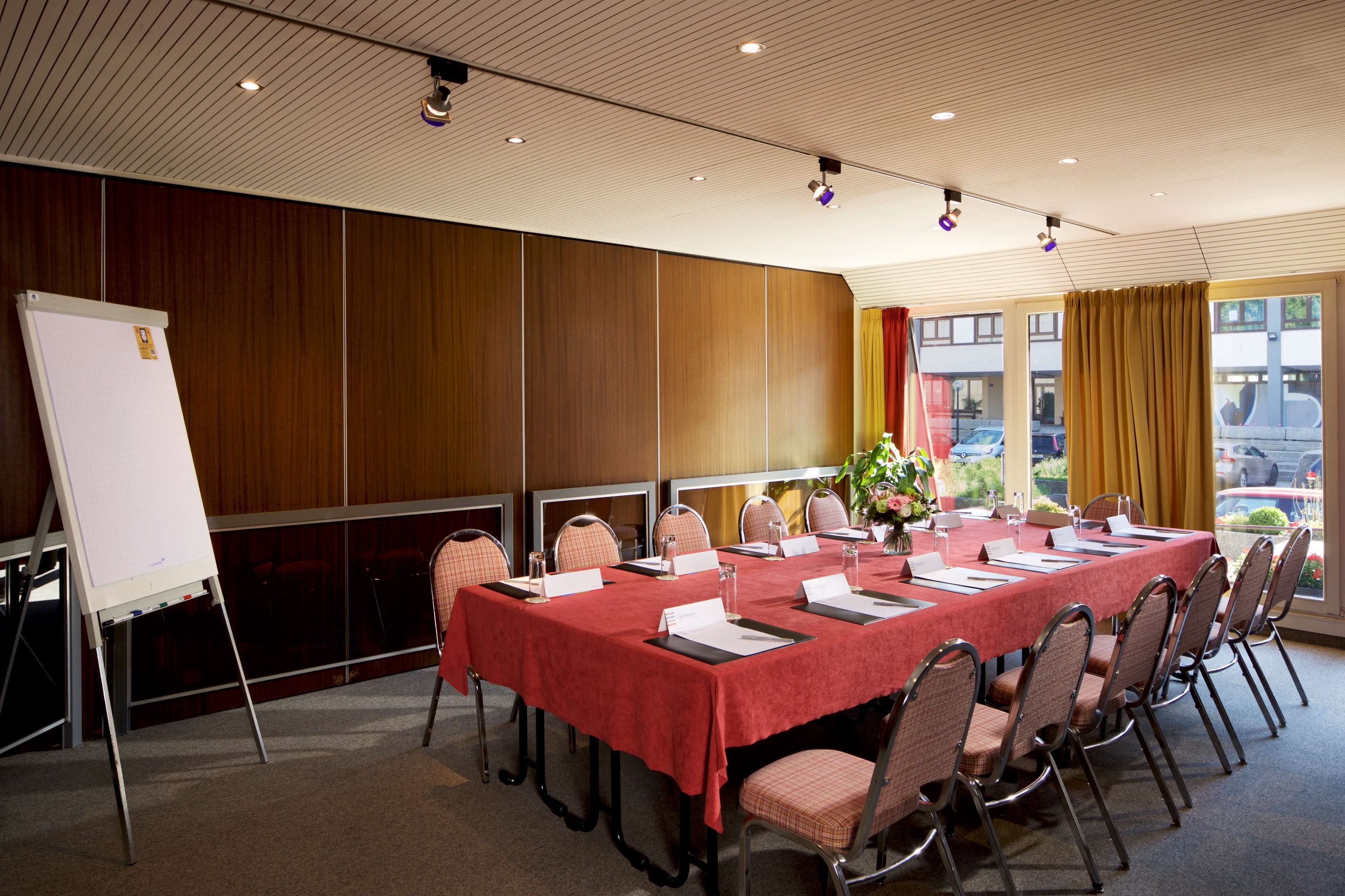 A conference room with a long table, chairs, a whiteboard, and a view of the outside.