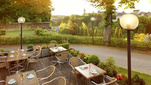 An outdoor café with tables and chairs, surrounded by greenery and a stone wall. - Hotel Parc Plaza (Luxembourg City)