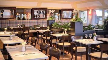 A restaurant with multiple tables and booths, each set with cutlery and a vase of flowers.