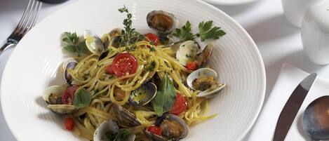 A plate of pasta with clams and vegetables, a wine glass, and salt and pepper shakers on a table.