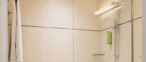 A modern bathroom with a glass-enclosed shower, a white bathtub, and a beige-tiled wall.