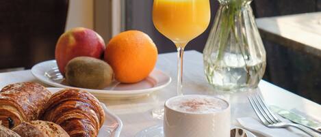 Una mesa de desayuno con croissants, frutas, un vaso de zumo de naranja y una taza de café.
