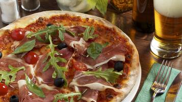 Une pizza garnie, un verre de bière et une serviette verte avec des couverts sur une table en bois.