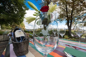 Una mesa al aire libre con una botella de vino, una copa y una rosa roja, junto a una cesta.
