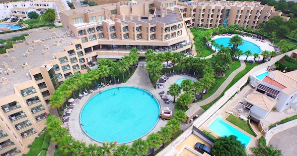 Una gran piscina rodeada de palmeras y un edificio de hotel de varios pisos con balcones.