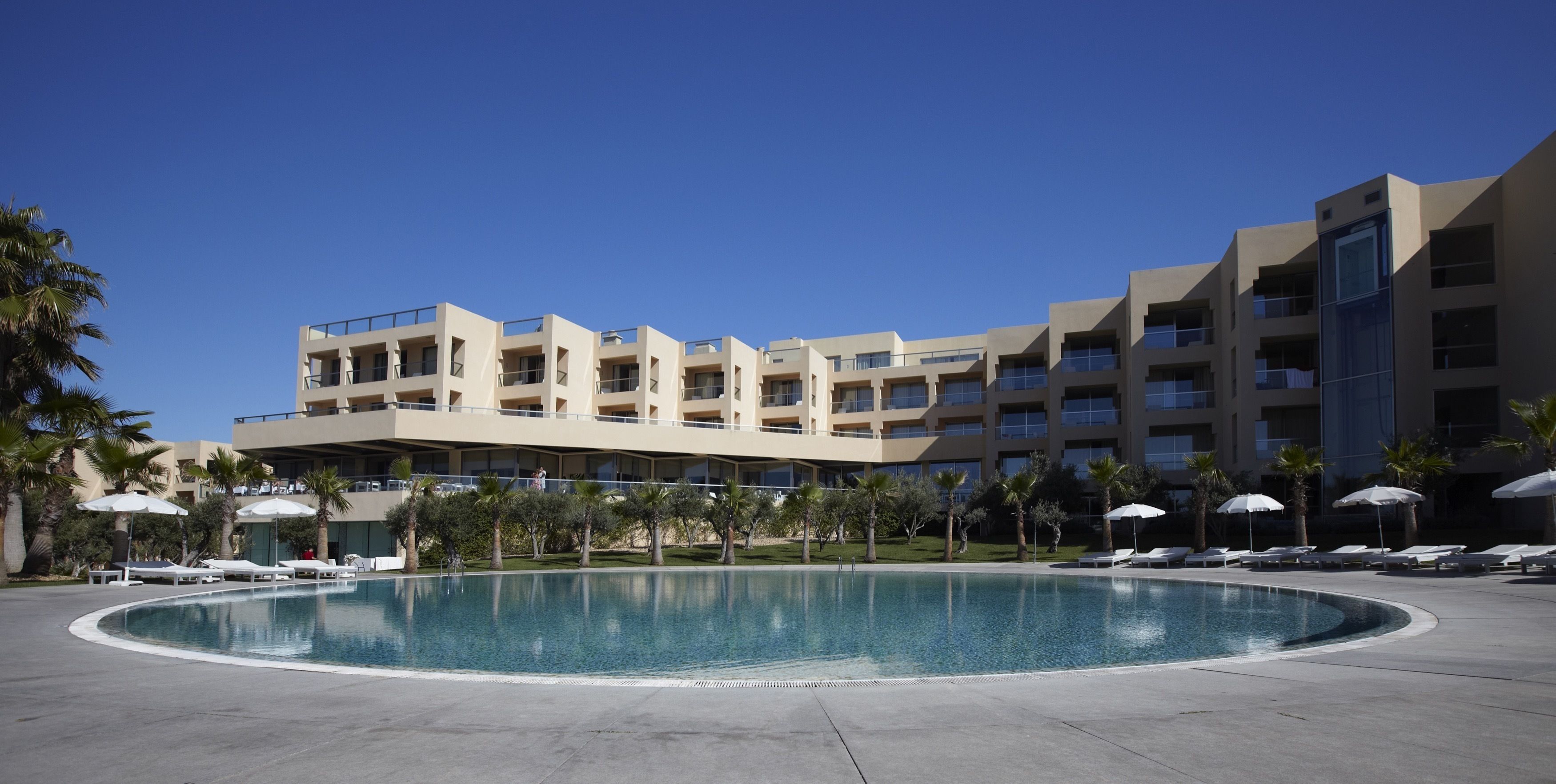 Un hotel moderno con una piscina grande, varios balcones y palmeras.