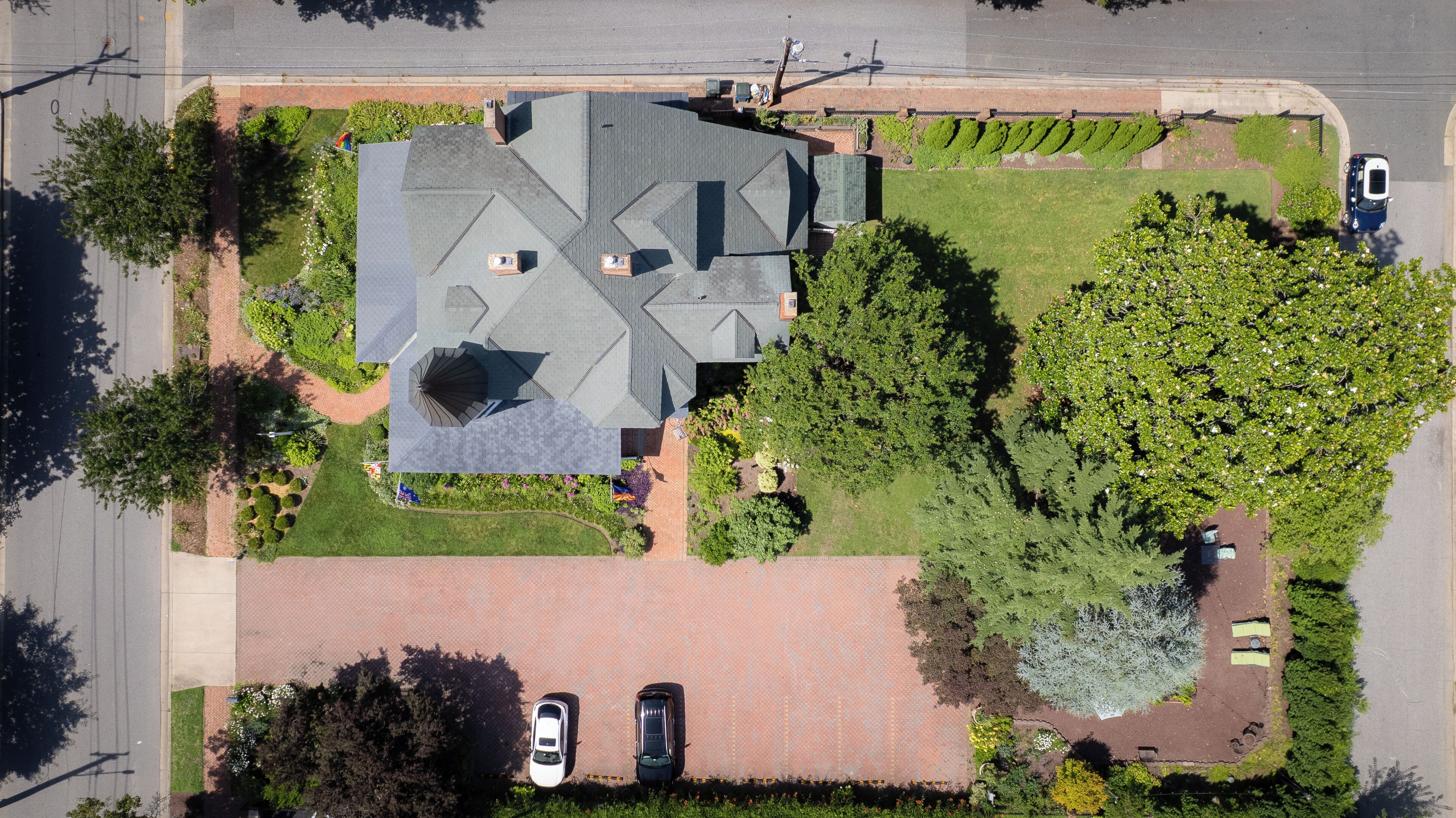 An aerial view of a residential area with a house, two cars parked in the driveway, and a well-maintained lawn.