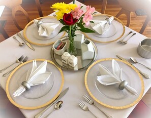 Ein Tisch für vier Personen, gedeckt mit goldfarbenen Tellern, Besteck und einer Blumenvase.