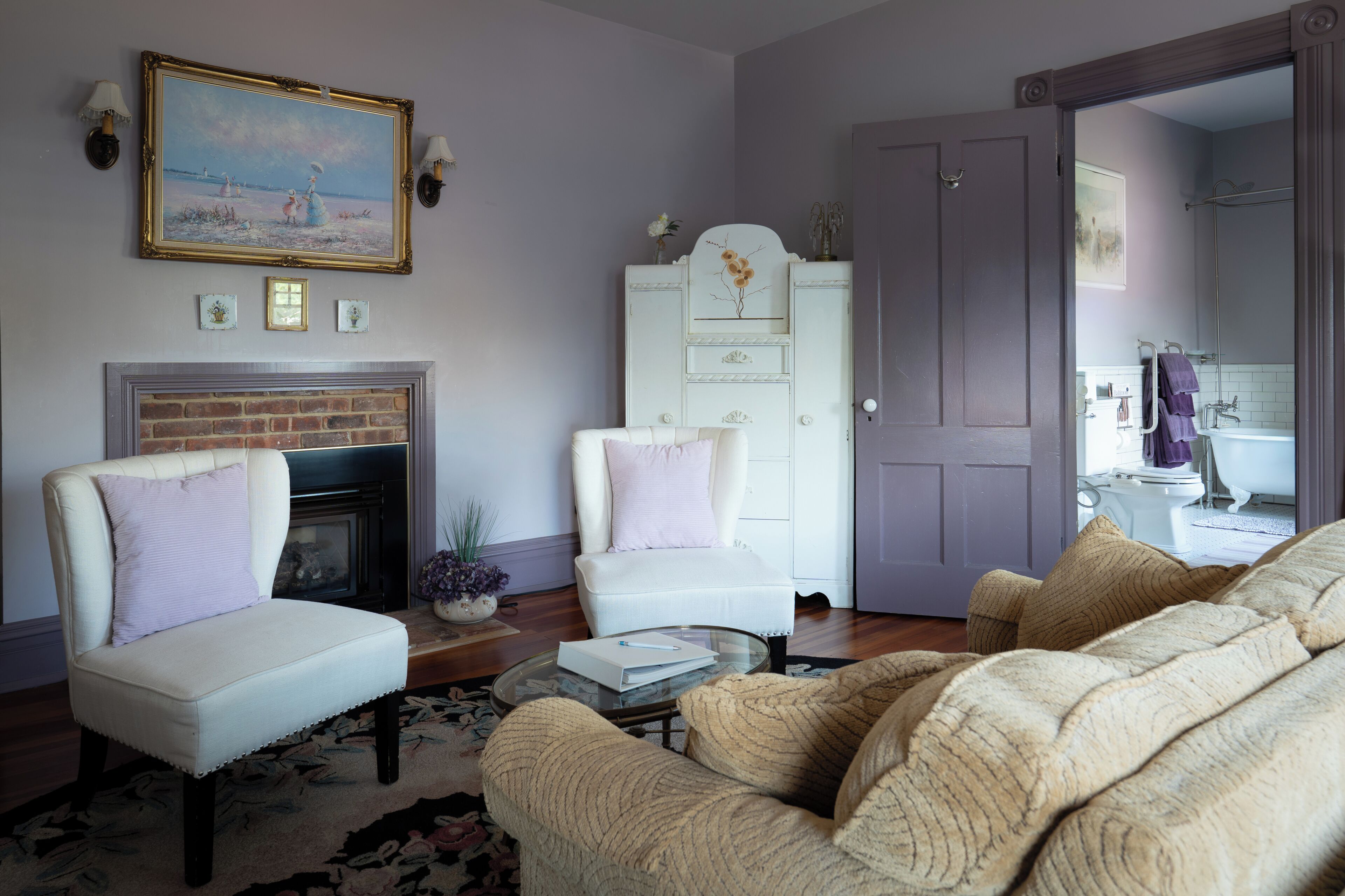 Una sala de estar con chimenea, un sillón blanco, un sofá y una puerta que da a un baño.