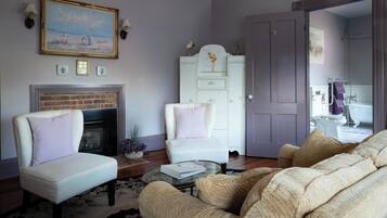 Una sala de estar con chimenea, un sillón blanco, un sofá y una puerta que da a un baño.