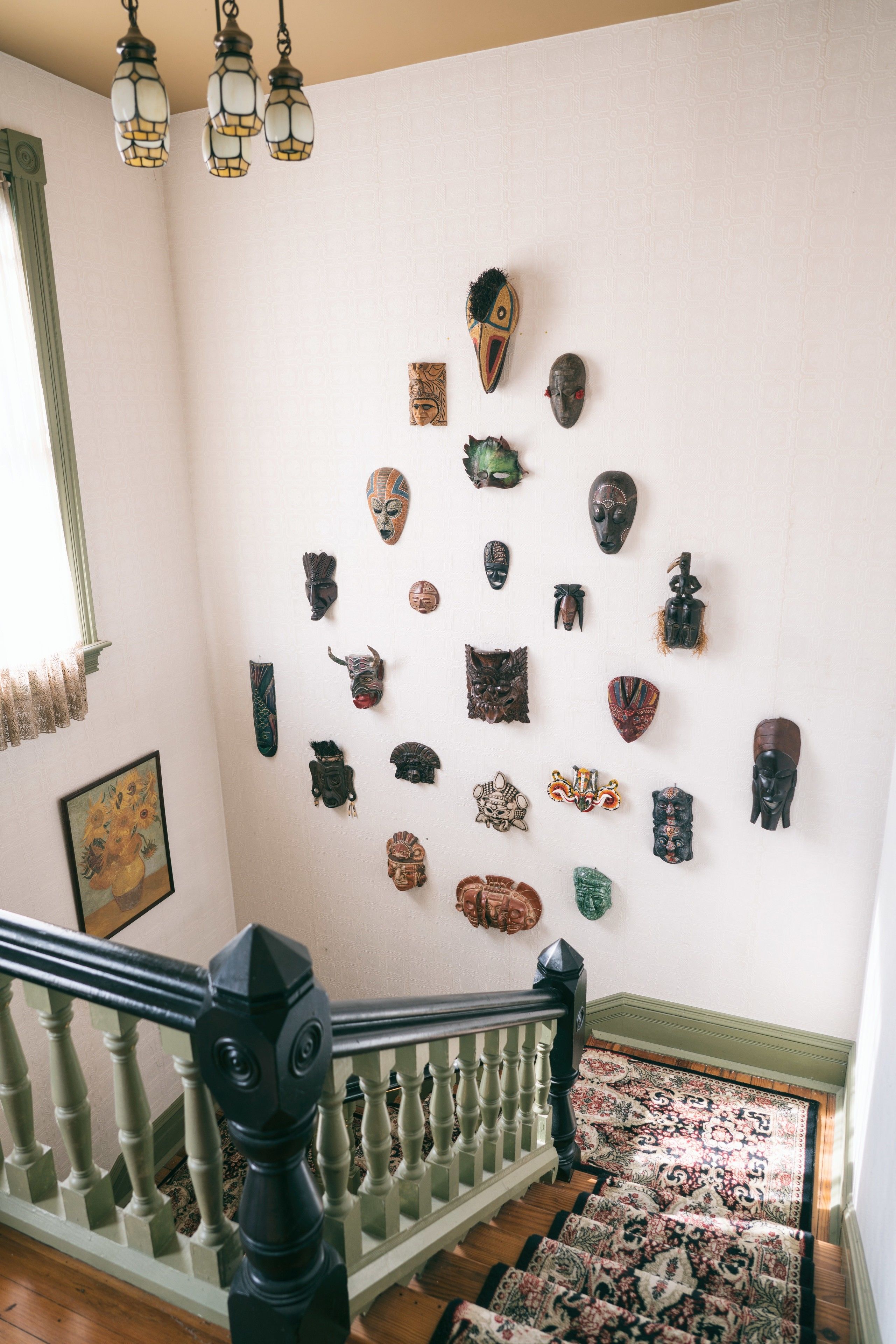 A staircase with a patterned carpet and a wall adorned with various masks.