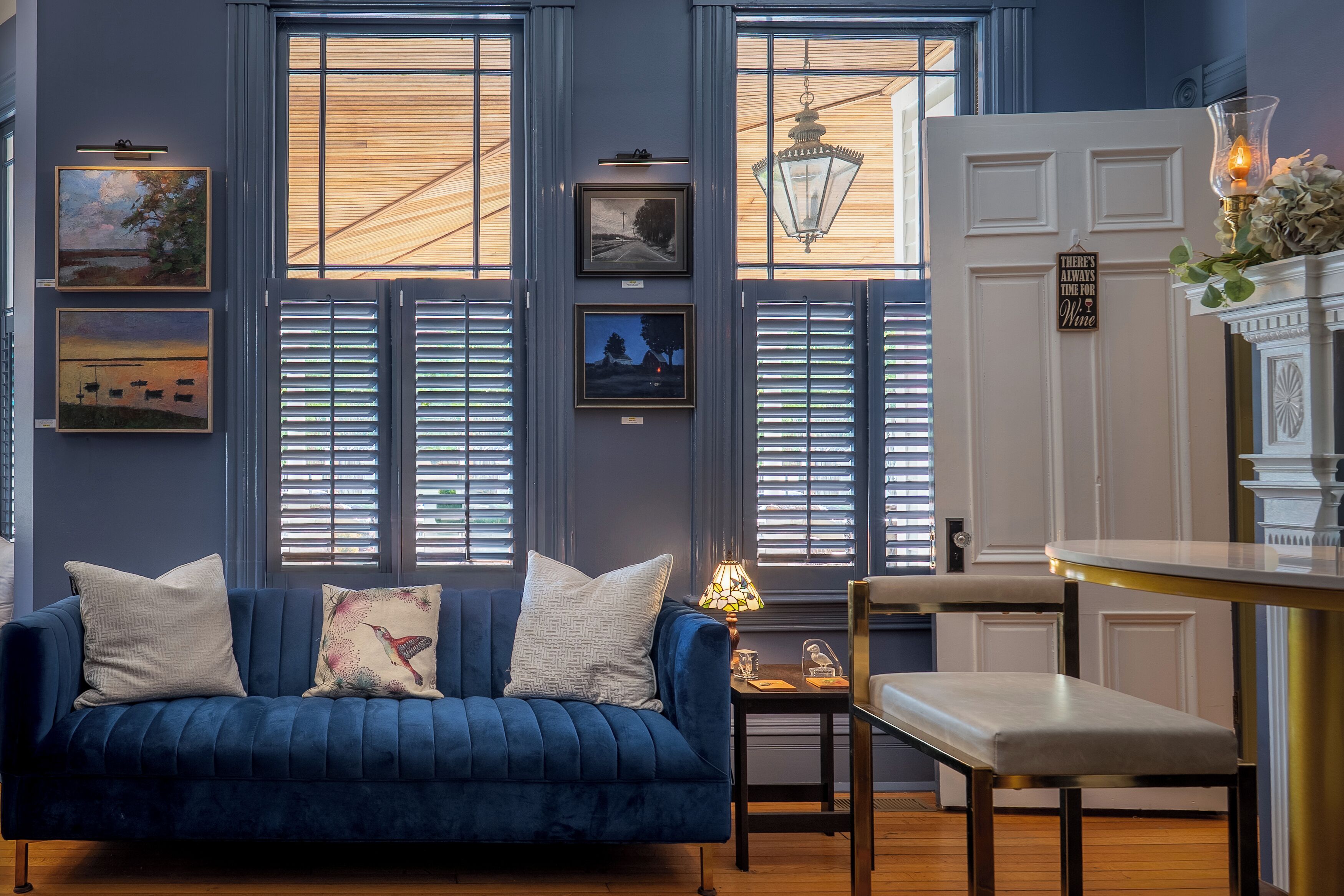 A room with a blue sofa, a dining table, and a chandelier. There are framed pictures on the wall and a sign that reads 'There's always time for wine.'