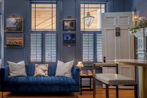 A room with a blue sofa, a dining table, and a chandelier. There are framed pictures on the wall and a sign that reads 'There's always time for wine.' - Hummingbird Inn (Easton)