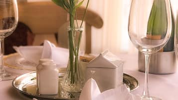 A table set with a clear glass vase containing flowers, a folded napkin, salt and pepper shakers, and a wine glass.