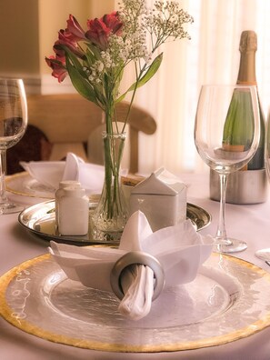 A table set with a clear glass vase containing flowers, a folded napkin, salt and pepper shakers, and a wine glass.