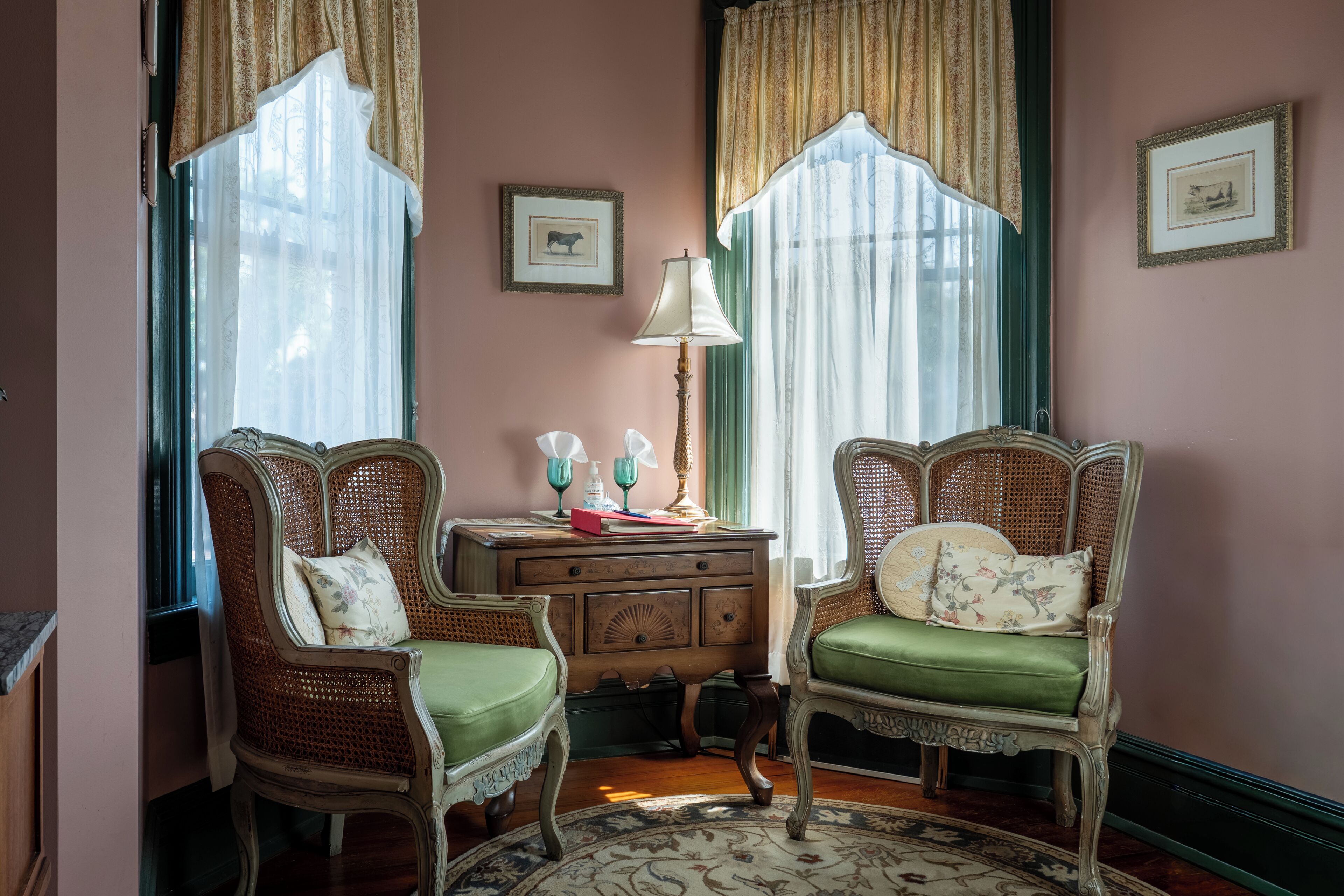 A room with two ornate wicker chairs, a wooden side table with a lamp, and a framed picture on the wall.