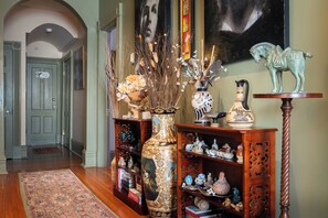 A hallway with a wooden floor, a rug, a bookshelf with decorative items, a vase with flowers, and a statue of a horse.