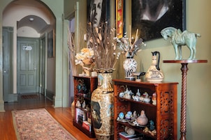 A hallway with a wooden floor, a rug, a bookshelf with decorative items, a vase with flowers, and a statue of a horse.
